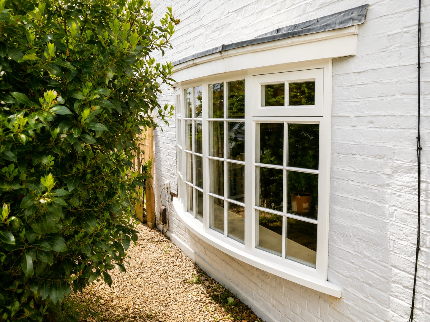 Cream timber curved bay casement window with glazing bars on a white painted brick cottage