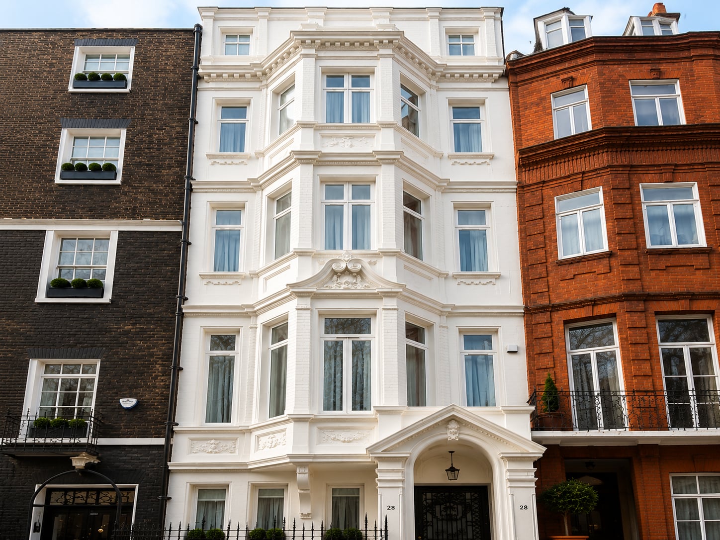 White stucco townhouse with tiered timber bay windows above a pillared entrance