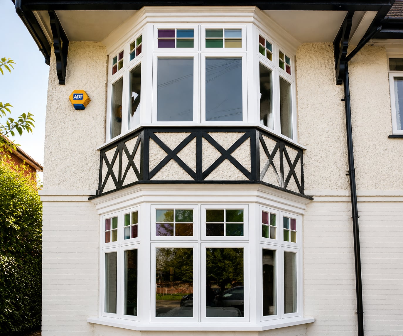 White timber bay casement windows with coloured leaded top lights beneath a black balcony rail