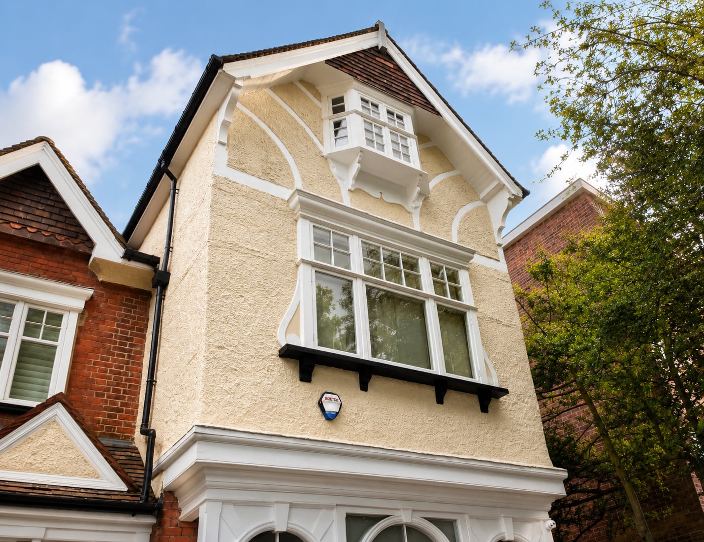 White timber casement windows with glazing bars in a cream rendered gable above a tiled bay roof