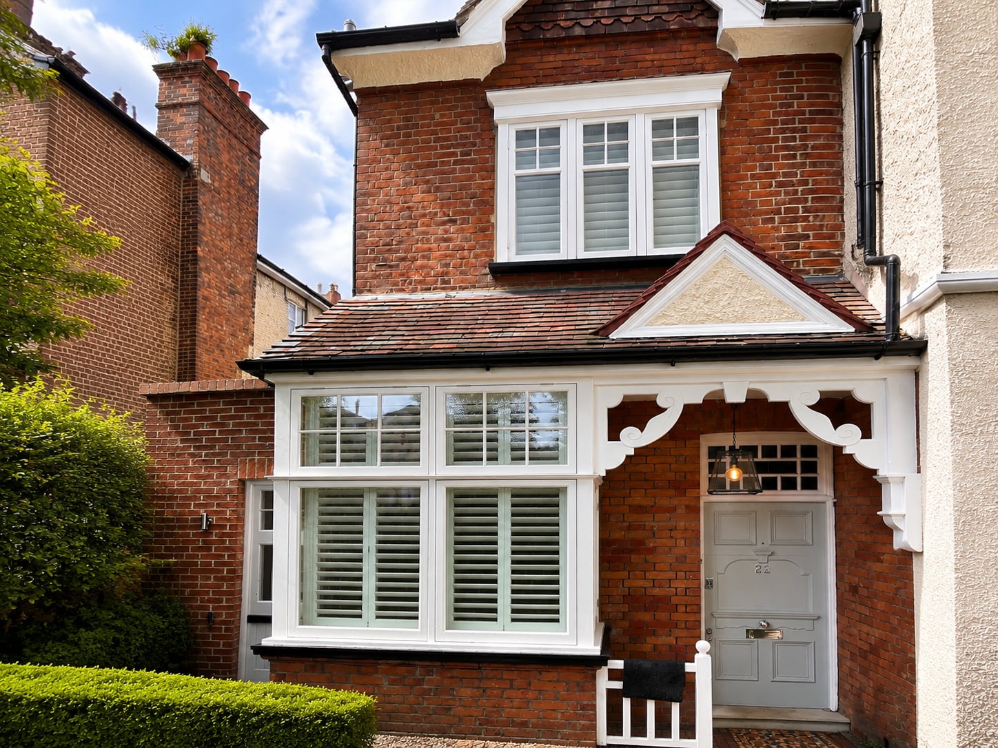 White timber casement bay window with interior plantation shutters on a red brick house