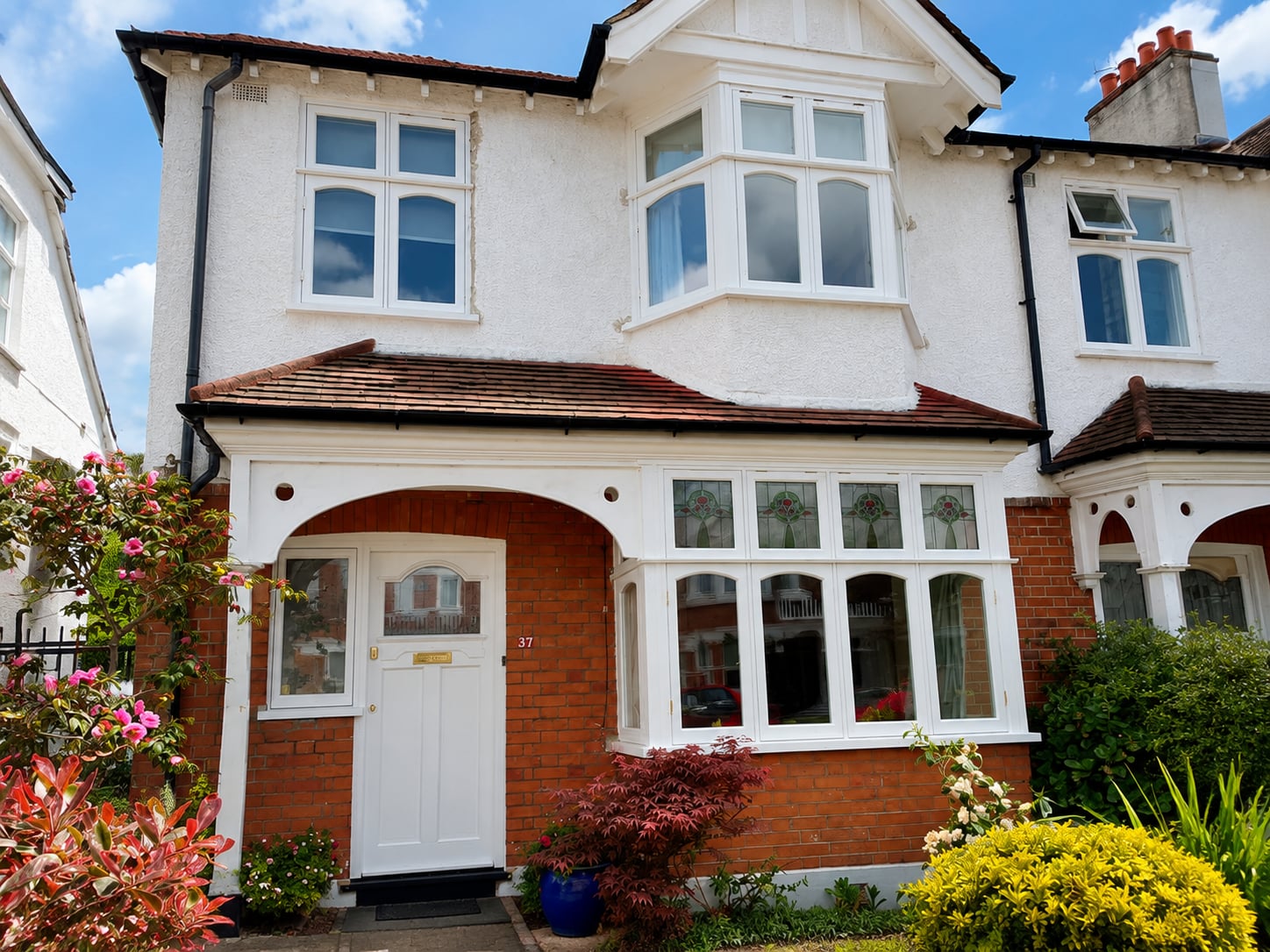 White timber casement and bay windows on a rendered house with an arched brick porch