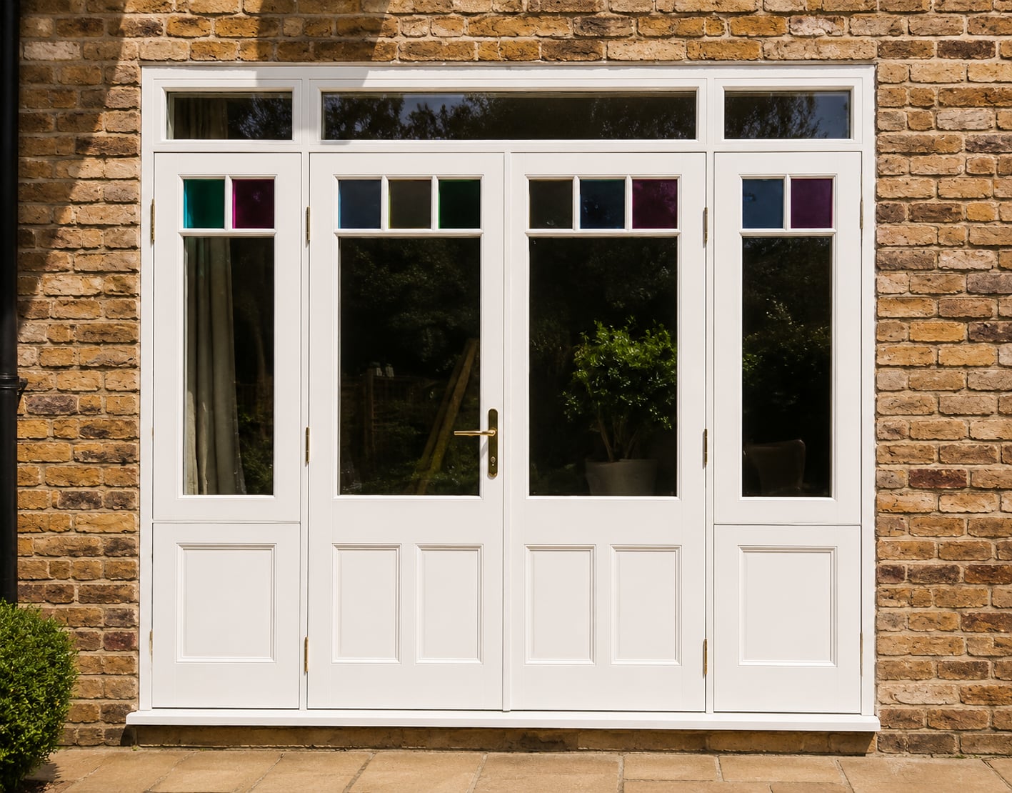 White timber French doors with side lights and coloured glass top lights in a stock brick opening