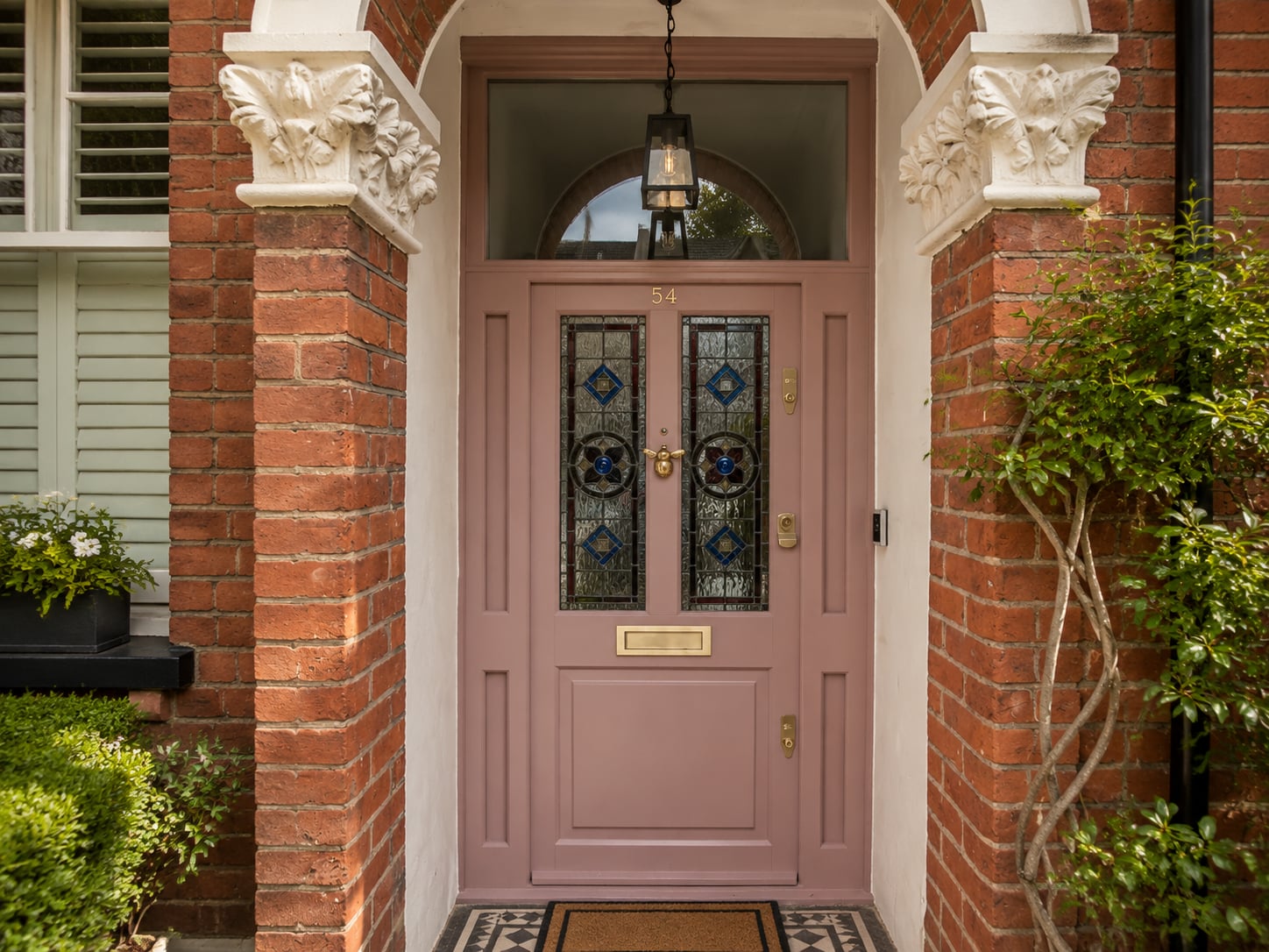 Dusty pink timber door with leaded stained glass panels beneath an arched fanlight