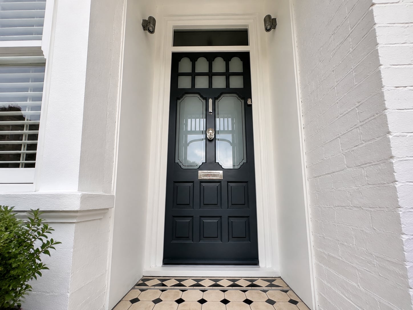 Black timber door with obscured glazed panels and coach lamps above a tiled step
