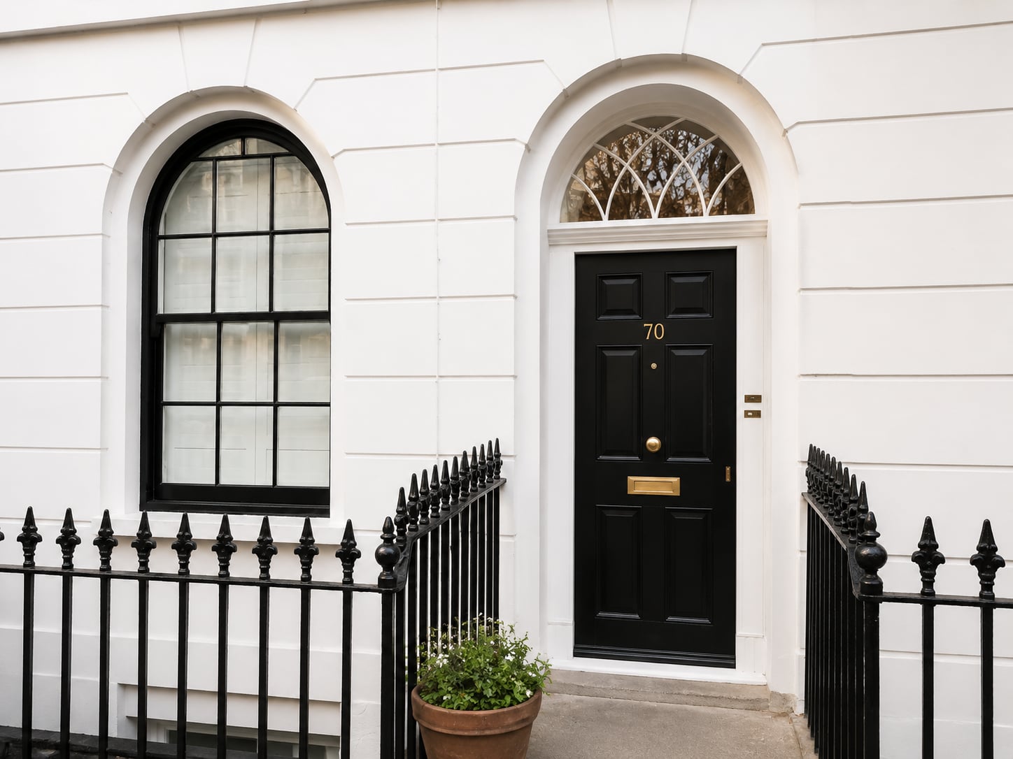 Black timber door with a radial fanlight beside an arched sash window on a white stucco terrace