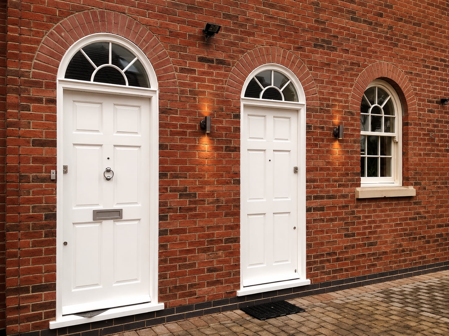 Two white timber doors with radial fanlights set in red brick arches
