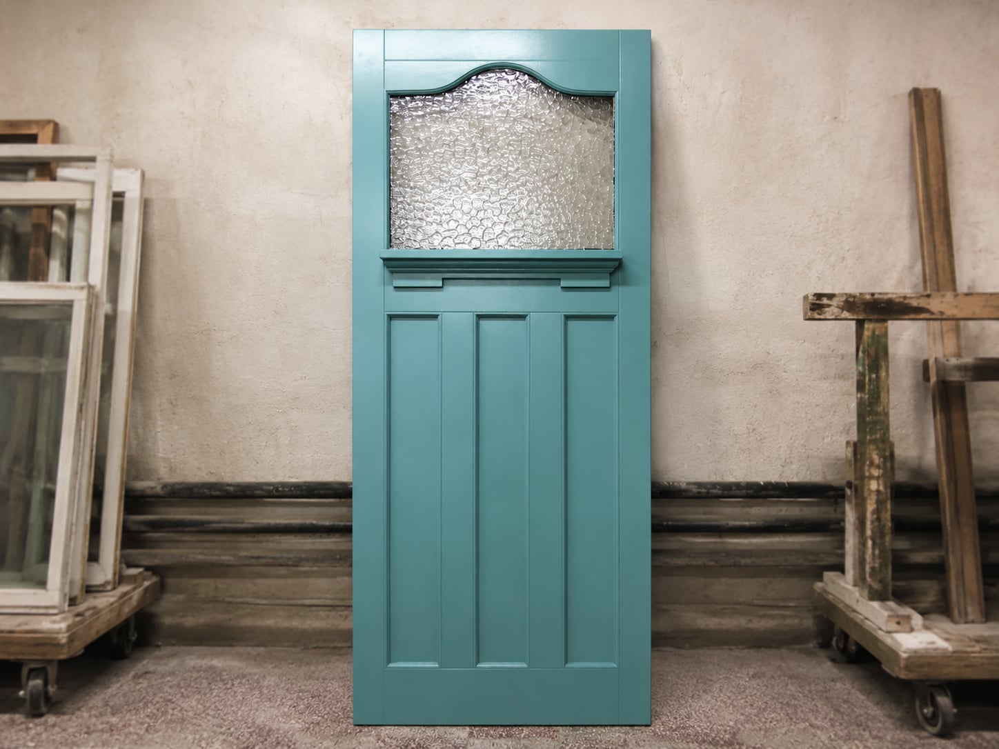 Teal panelled timber door with an obscured glass top panel, photographed in the workshop