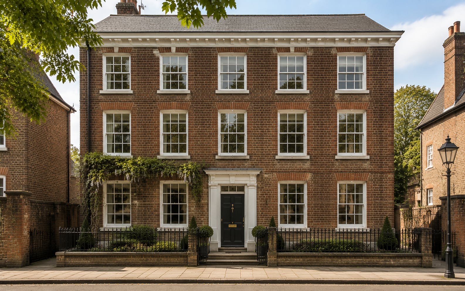 Three storey Georgian brick townhouse in Winchester with white timber six over six sash windows and a black door beneath a fanlight